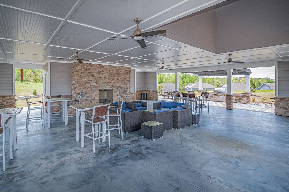 Large covered outdoor pavilion with a stone fireplace, ceiling fans, wicker seating, and bar tables on a stained concrete patio