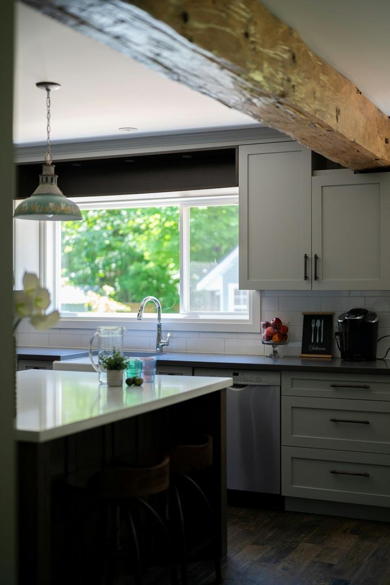Bright kitchen with a massive reclaimed wood beam overhead, white shaker cabinets, an island, and a garden view through the window