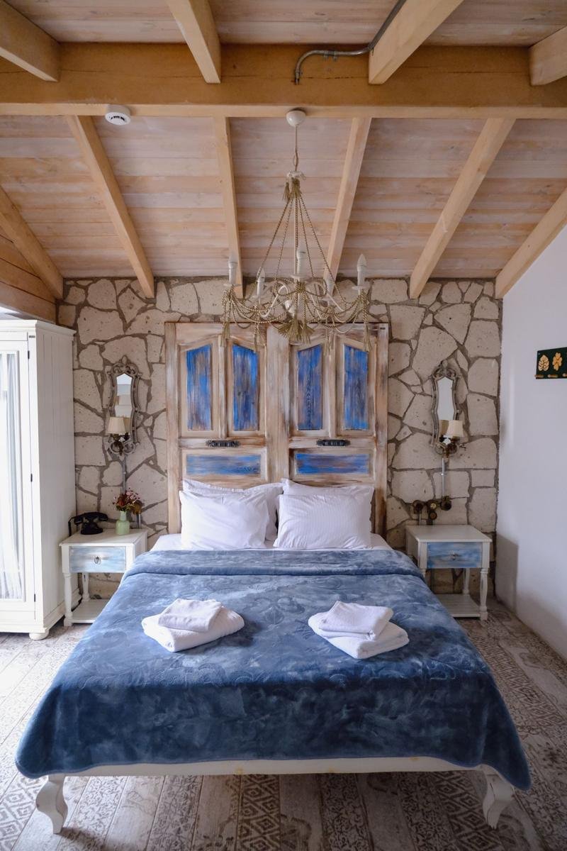 Rustic bedroom with exposed wood beam ceiling, a natural stone accent wall, and a bed dressed in a blue coverlet